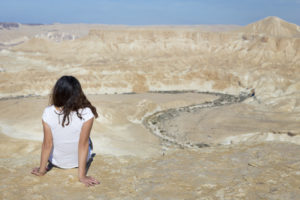 Woman sitting desert mountain edge.